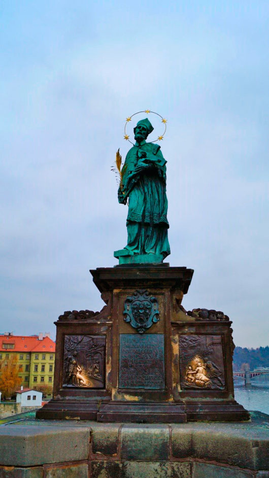 Estátua de São João de Nepomuceno na Ponte Carlos, com detalhes aos pés que mostram o momento em que ele estava sendo jogado no rio